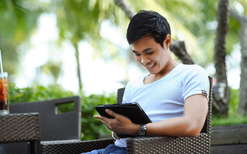 A man outdoors smiling as he uses a tablet, likely accessing an All in One Digital Marketing Platform, demonstrating the convenience of managing marketing tasks on the go.