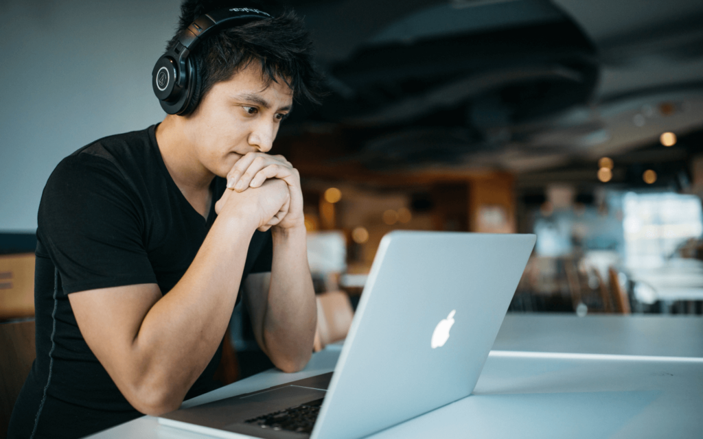 Concentrated marketer with headphones analyzing email marketing performance metrics on a laptop in a busy café environment, reflecting dedication to improving campaign effectiveness.