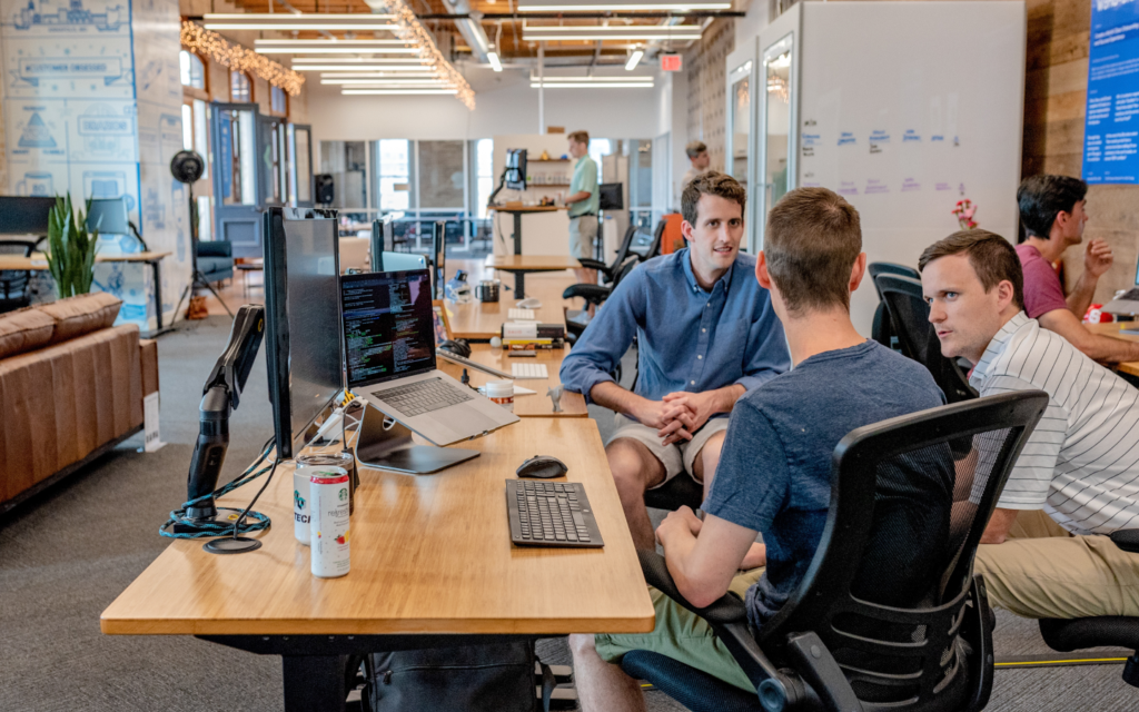 Tech team collaborates on analyzing email marketing performance metrics, surrounded by computers and whiteboards in an open-plan office.