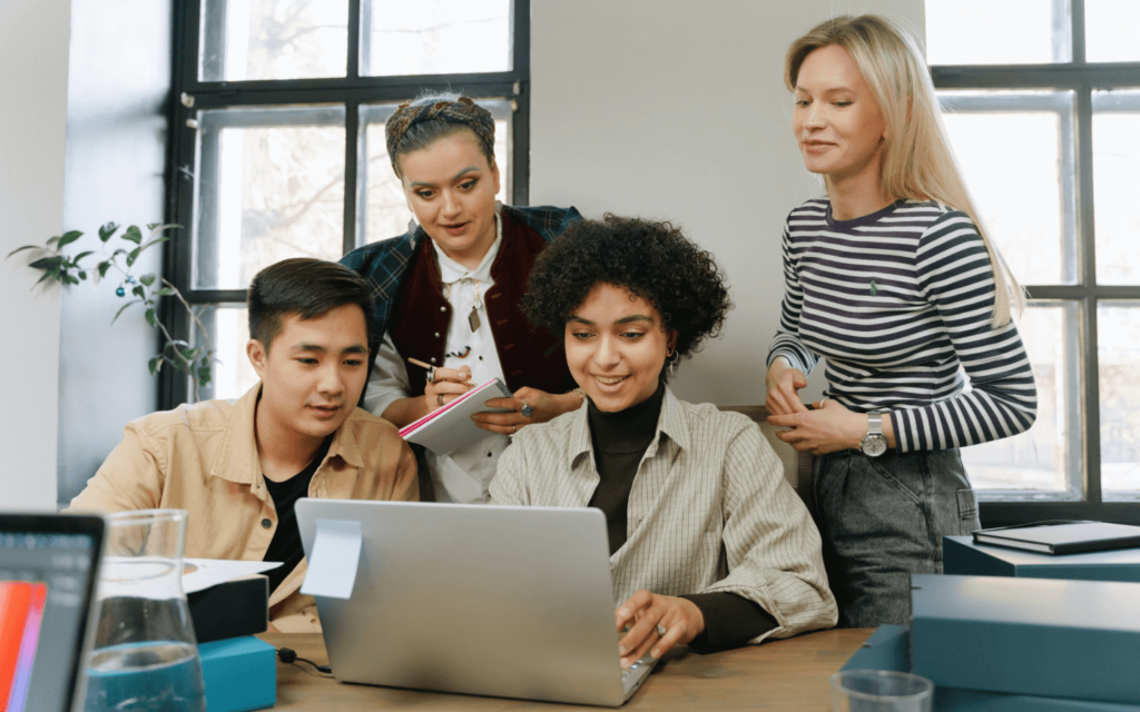 A team of four professionals collaboratively working on reporting best practices with a laptop and notebooks in a well-lit office space.