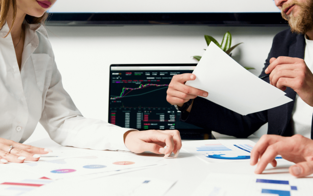 Two financial professionals analyzing data charts and a computer screen displaying market trends, emphasizing reporting best practices in a corporate setting.