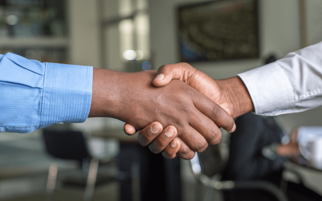 Two professionals shaking hands in an office setting, representing the successful discussion and implementation of reporting best practices.