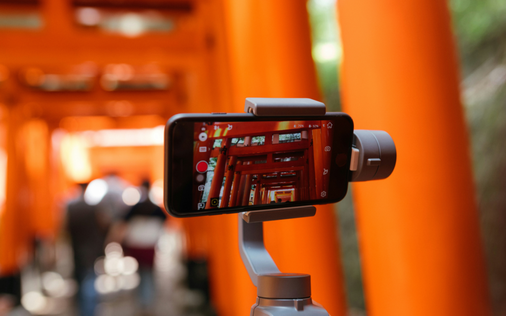 Smartphone on a gimbal capturing live video of red torii gates for digital marketing content, showcasing the integration of technology in storytelling and audience engagement.