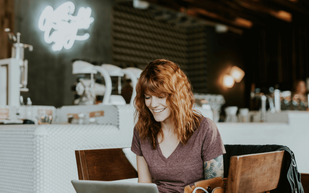 Smiling digital marketing professional working on a laptop in a café, exemplifying the modern, mobile, and flexible lifestyle of today's digital marketers.