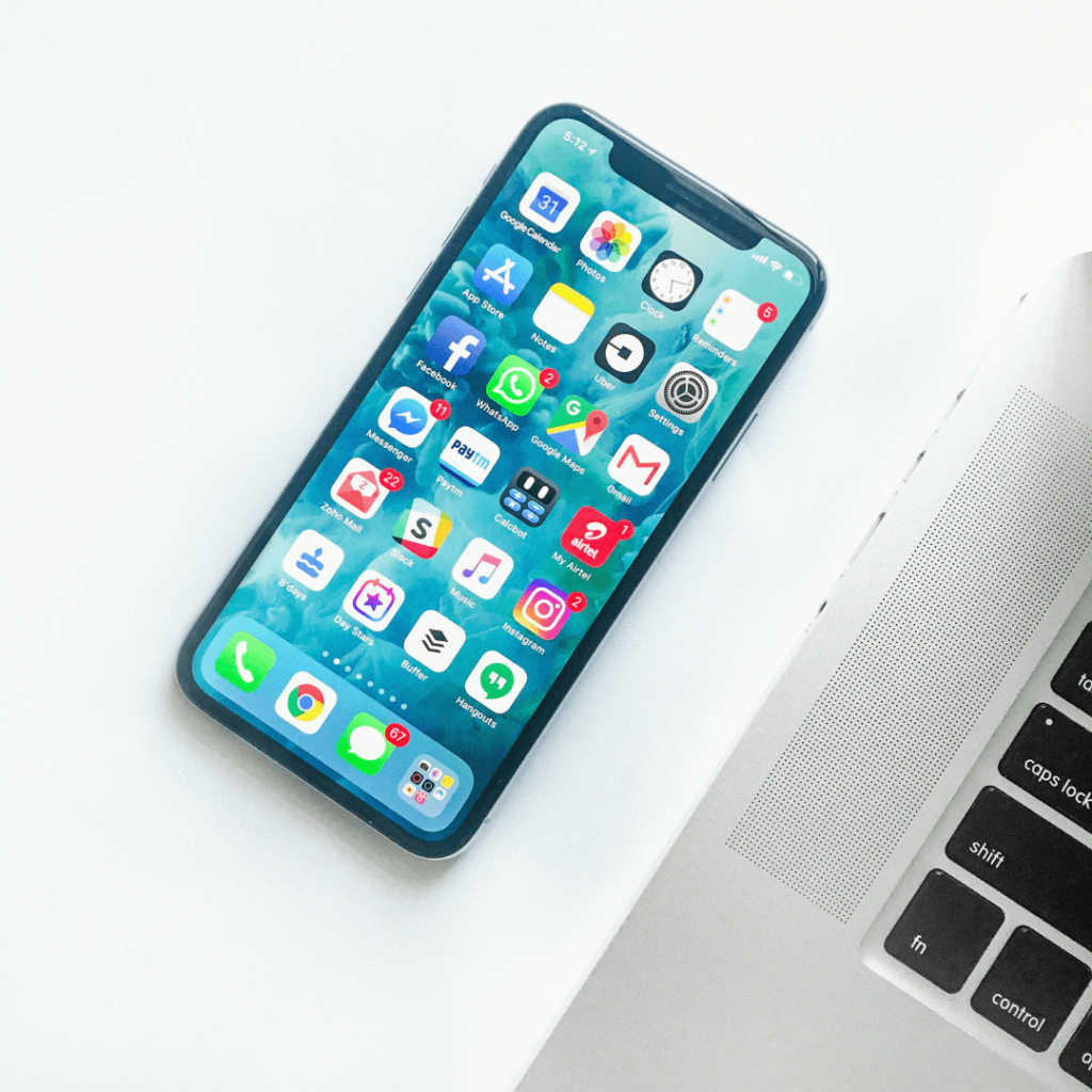 Smartphone with social media applications on screen, essential for influencer marketing strategies, beside a laptop on a white desk.