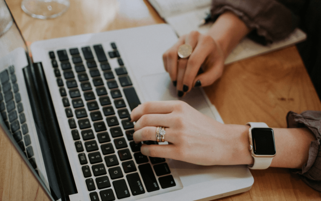 Close-up of a marketer's hands typing on a laptop, with a smartwatch visible, representing the active lifestyle of an influencer marketing expert.