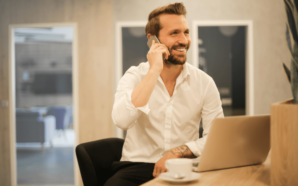 Smiling professional man on a phone call at his desk with a laptop, potentially offering insights on a White Label SEO Report Generator to a client