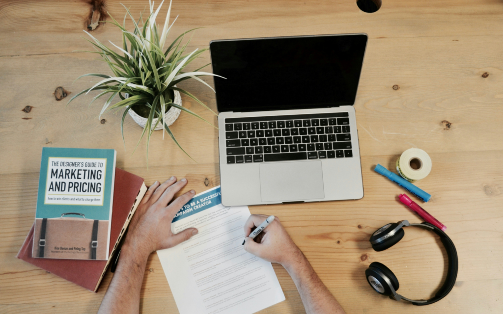 Overhead view of a digital marketer's desk with a laptop, marketing book, headphones, and office supplies, emphasizing continuous learning and organization in digital marketing.