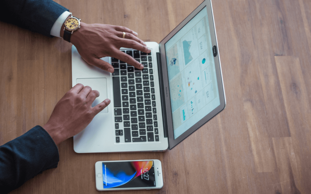 A person examining a website SEO report on a laptop with analytical graphs, alongside a smartphone, on a wooden desk.