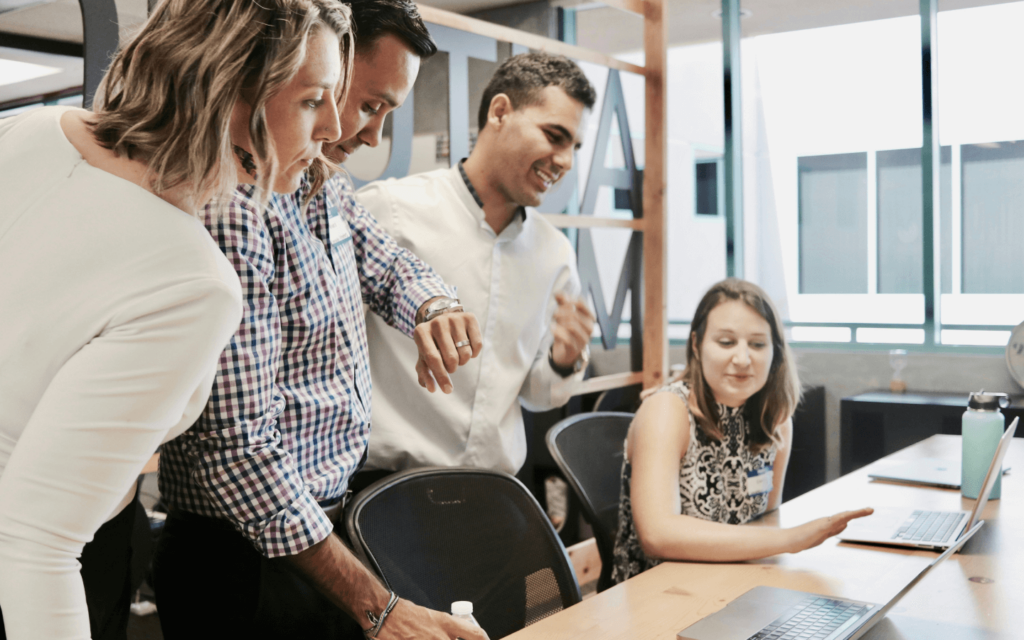 A group of colleagues collaboratively focusing on a laptop, indicative of an 'Affiliate Marketing for Beginners' workshop in a modern office setting.