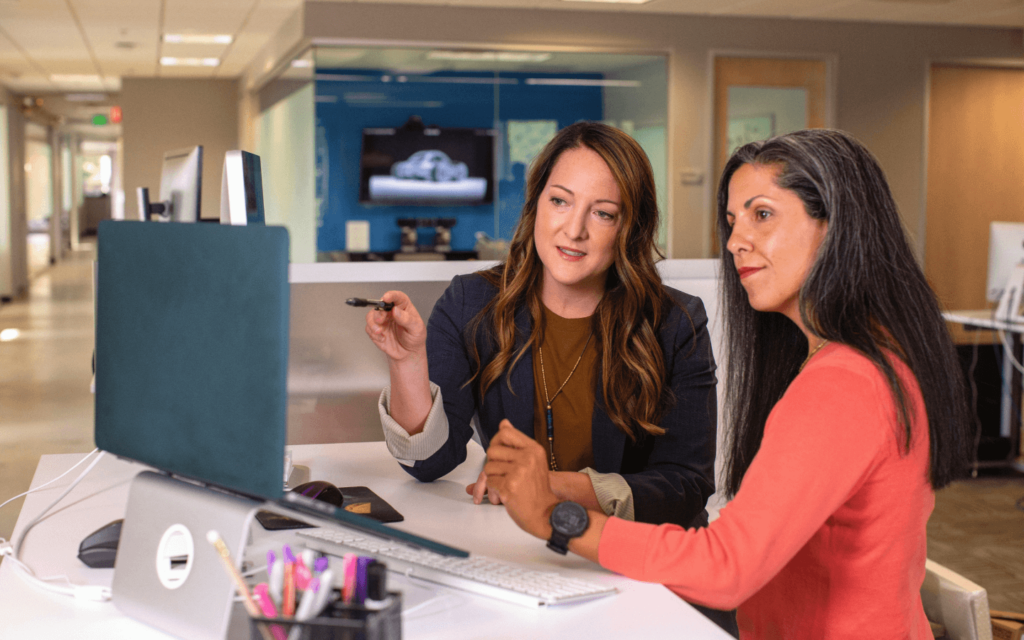 Two office professionals engaged in a discussion over a computer screen, using Client Reporting Software to explore and interpret client analytics in a collaborative setting.