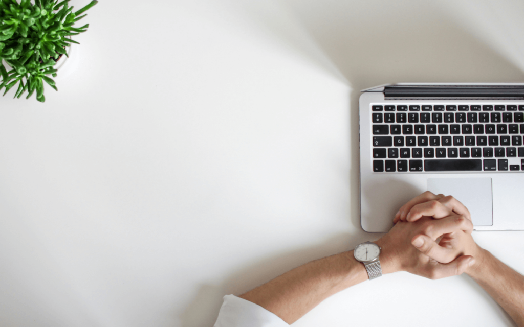 Overhead view of a person at a white desk with a laptop and a potted plant, possibly contemplating strategies for a website SEO report.