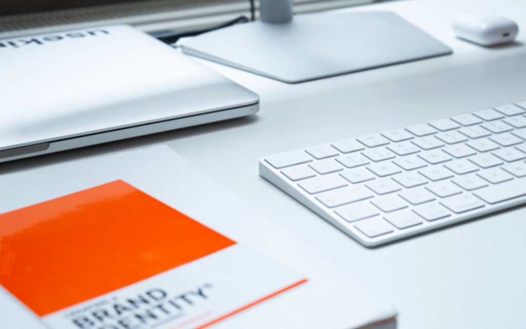 A modern workspace with white label SEO reporting dashboard essentials, including a white keyboard, computer mouse, and a brand identity document with an orange cover.