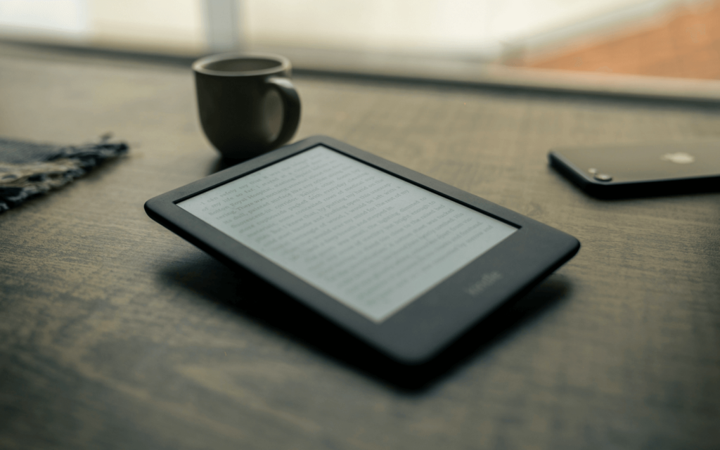 An e-reader displaying a page possibly about lead magnets, on a wooden surface beside a cup of coffee and a smartphone, representing a serene reading setup.