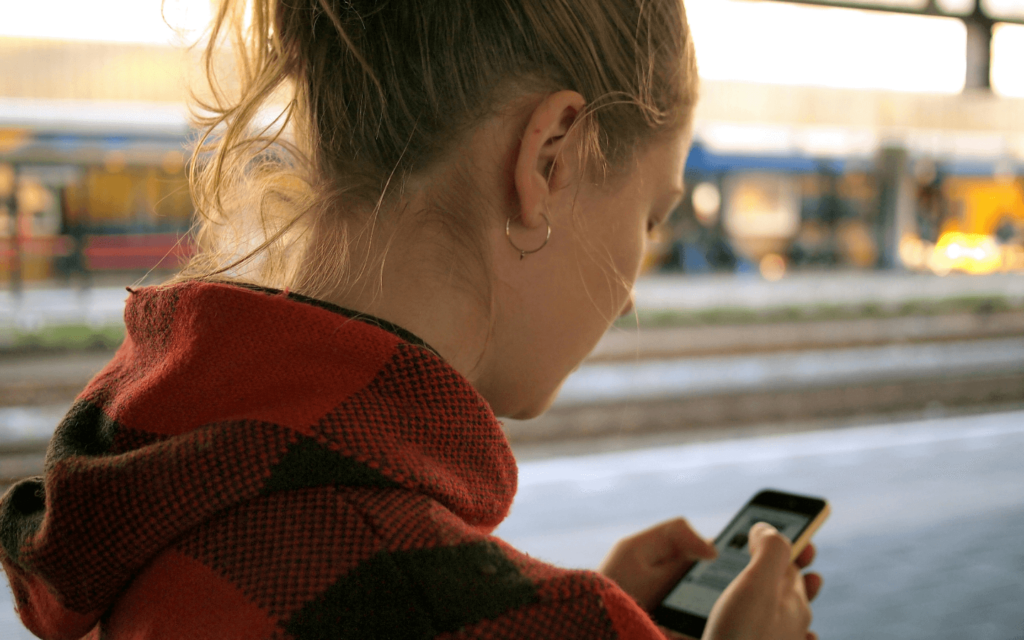 A woman at a train station absorbed in her smartphone, potentially interacting with a lead magnet, showcasing the effectiveness of mobile marketing.